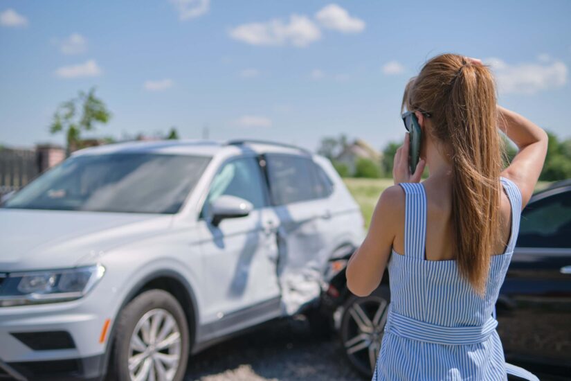 Shocked female driver talking in a car on the road near her wrecked vehicle asking for emergency help after a car accident.